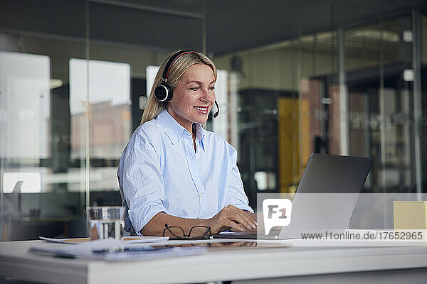 Smiling businesswoman wearing headset using laptop at desk in office