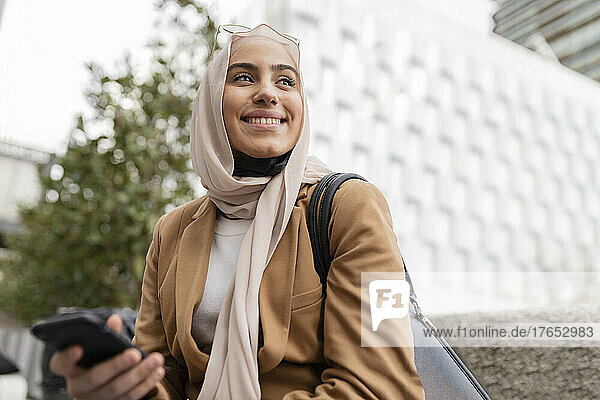 Smiling young businesswoman with mobile phone at office park