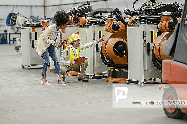 Engineer pointing at robotic arm discussing with businesswoman holding tablet PC in factory