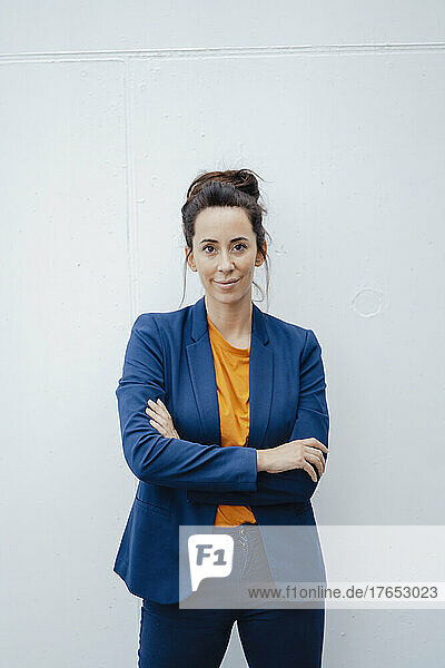 Confident businesswoman with arms crossed standing in front of white wall