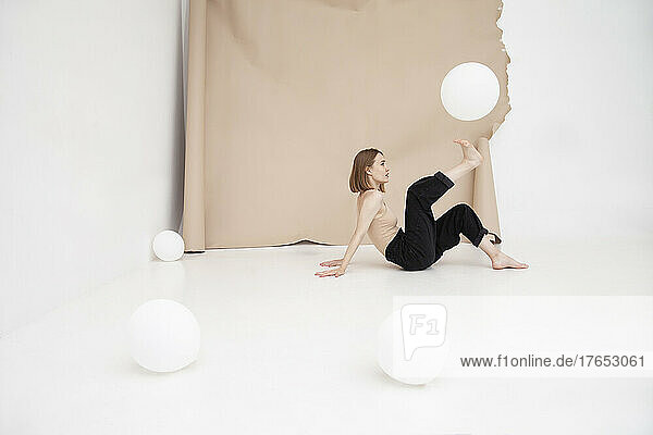 Young woman playing with balloon against brown backdrop