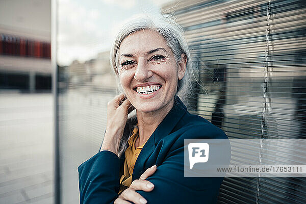 Cheerful businesswoman with gray hair by glass wall
