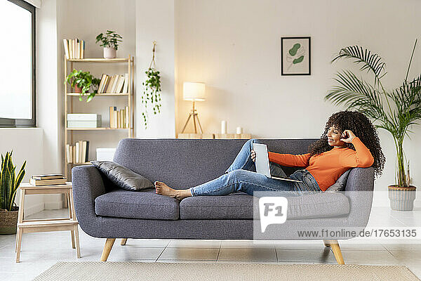 Young woman with laptop sitting on sofa in living room at home