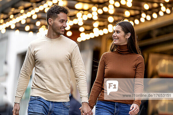Smiling couple walking with holding hands in front of illuminated ceiling