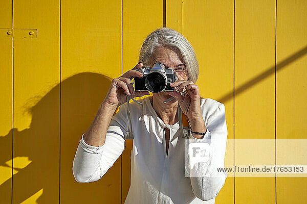 Woman photographing with camera standing in front of yellow door