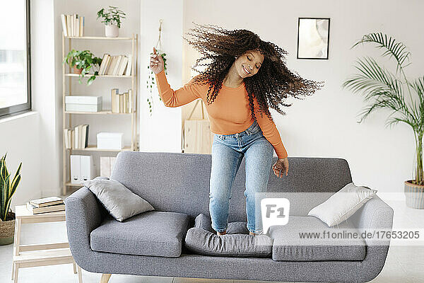 Smiling woman with tousled hair dancing on sofa at home