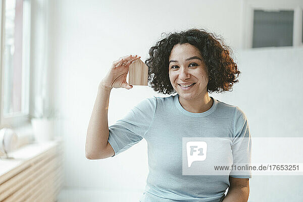 Happy woman with curly hair holding model house at home