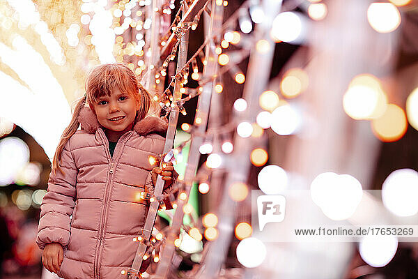 Lächelndes süßes Mädchen  das Weihnachtsbeleuchtung bereitsteht