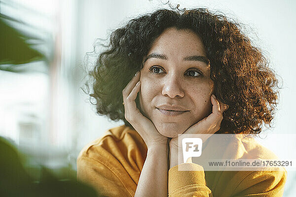 Thoughtful woman with curly hair sitting with head in hands at home