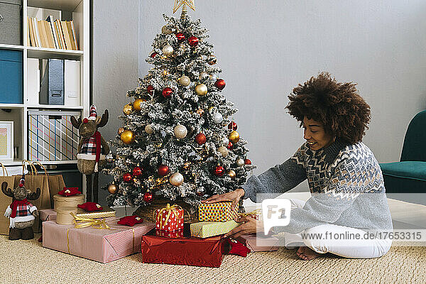 Smiling woman arranging gifts by Christmas tree at home