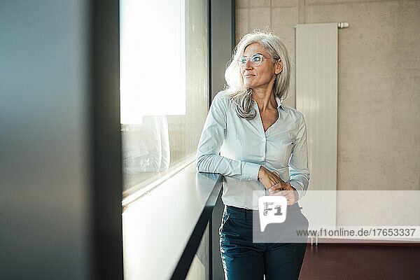 Geschäftsfrau mit Brille blickt im Büro durchs Fenster