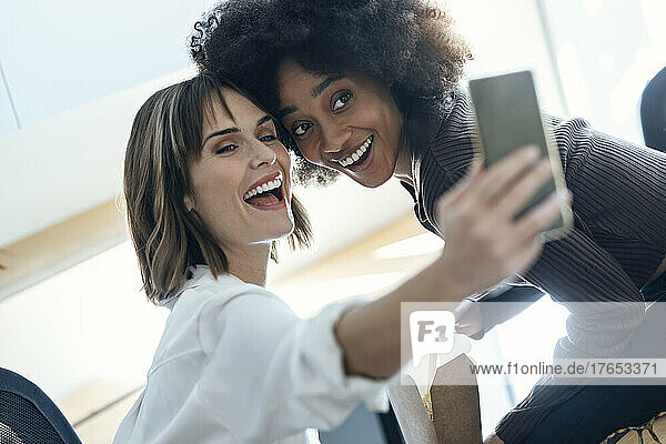 Happy businesswoman taking selfie with colleague through mobile phone in office
