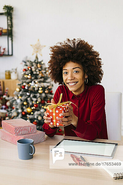 Glückliche Frau mit Weihnachtsgeschenken sitzt zu Hause mit Tablet-PC