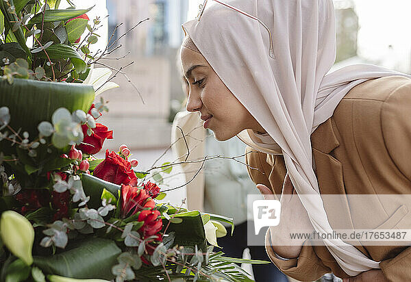 Young woman wearing hijab smelling flowers