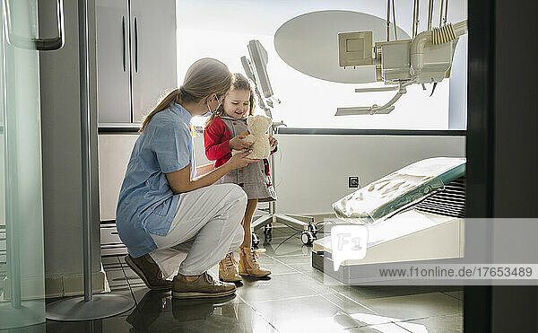 Dentist crouching by cute little girl at dental clinic