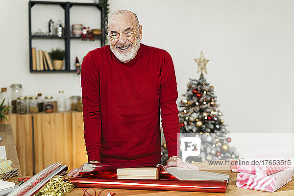 Glücklicher älterer Mann mit Geschenkpapier und Schachteln auf dem heimischen Tisch