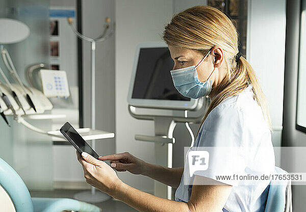 Dentist with protective face mask using tablet PC at dental clinic