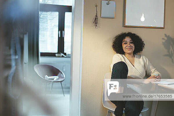 Smiling woman with coffee cup and tablet PC sitting on chair at home