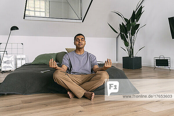 Mann mit geschlossenen Augen meditiert zu Hause vor dem Bettzeug