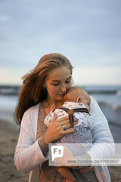 Young blond woman carrying son on beach at sunset