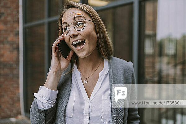 Happy woman talking on mobile phone in front of building