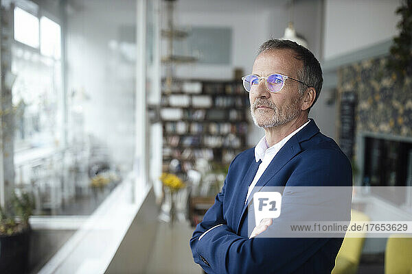 Businessman wearing eyeglasses standing with arms crossed in cafe