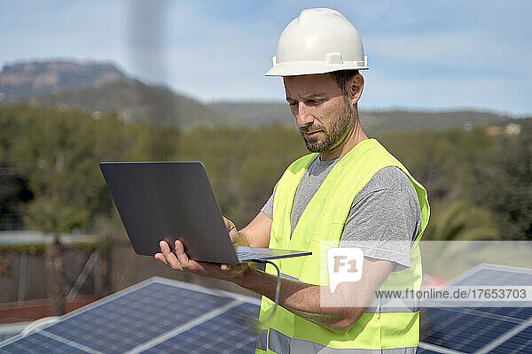 Engineer wearing hardhat using laptop on sunny day
