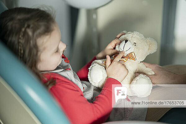 Little girl sitting on dental chair with stuffed toy at medical clinic