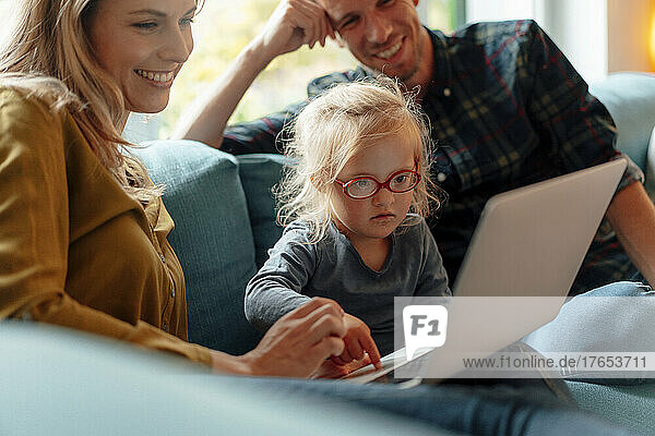 Lächelnder Vater und Mutter schauen Tochter mit Laptop an  die zu Hause auf dem Sofa sitzt