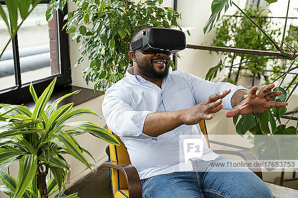 Smiling businessman wearing virtual reality simulator sitting on chair in office