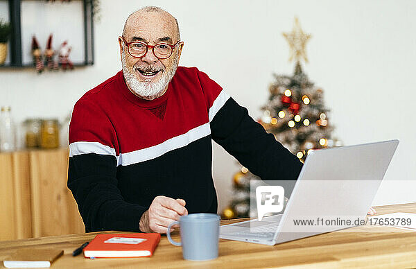 Smiling senior man with laptop sitting at home