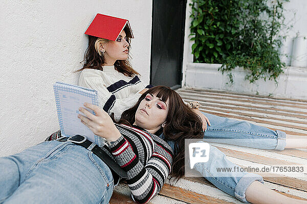 Woman reading book lying on bored friends lap