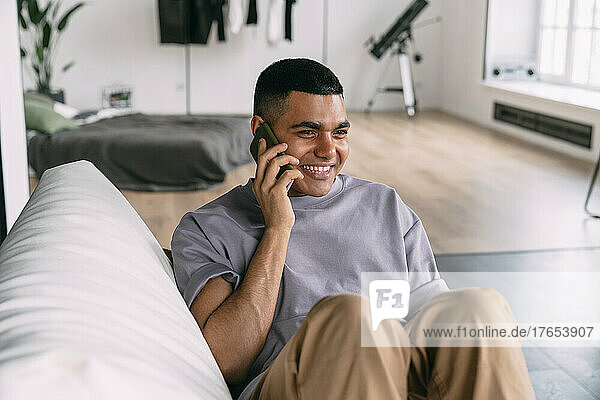Smiling man talking on mobile phone sitting on sofa at home