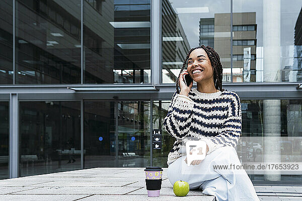 Happy young businesswoman talking on mobile phone at office park