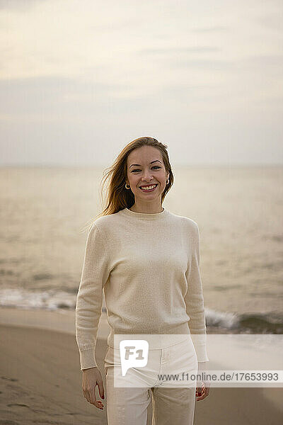 Smiling woman standing on beach in front of Baltic sea at sunset