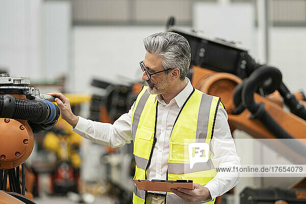 Technician holding file folder checking robotic arm in warehouse