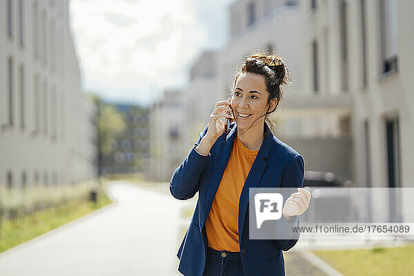 Smiling businesswoman talking on mobile phone standing on footpath