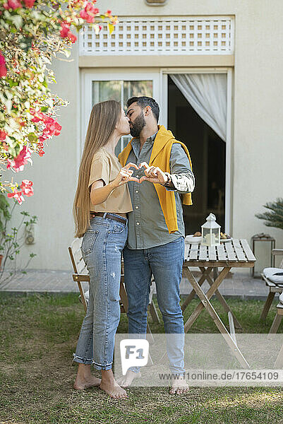 Couple kissing and showing heart sign with hands in back yard garden