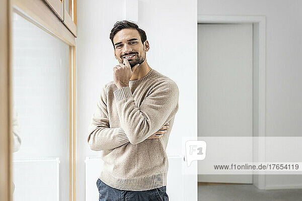 Smiling man with hand on chin standing near window at home