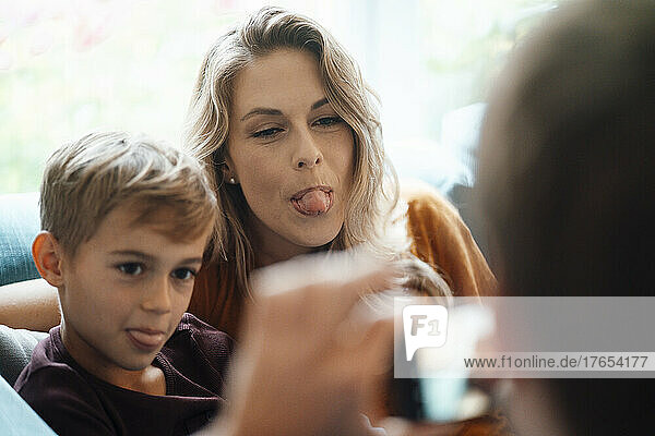 Blonde Frau mit ihrem Sohn  der die Zunge herausstreckt  fotografiert von einem Mann zu Hause