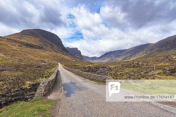 Empty applecross pass road with mountains in background under cloudy sky