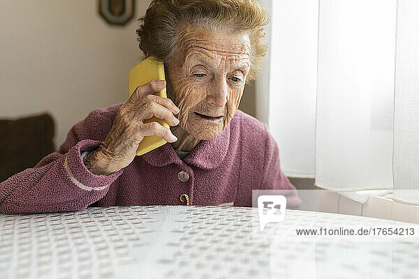 Senior woman with brown hair talking on mobile phone sitting at dining table