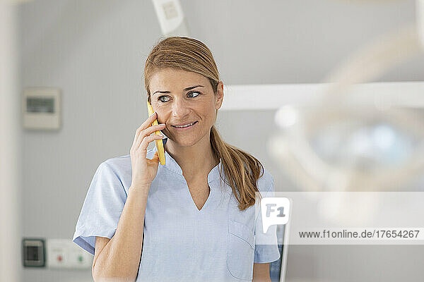 Smiling blond dentist talking on mobile phone at medical clinic