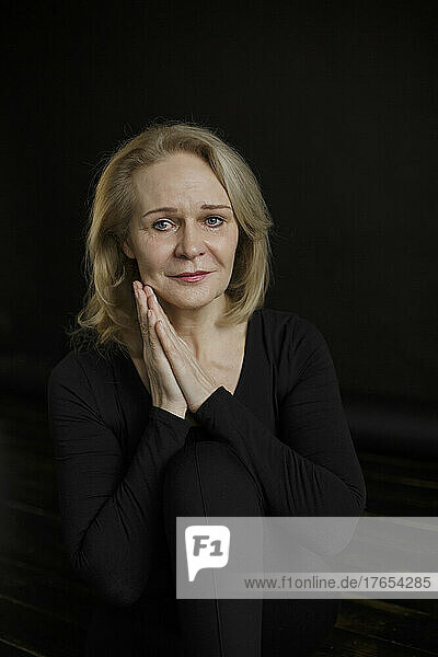 Sad woman with blond hair sitting against black background