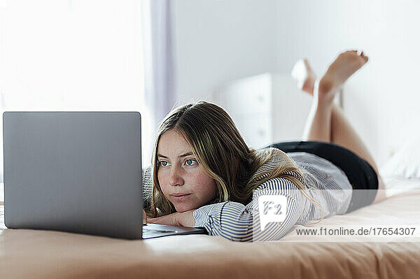 Young woman using laptop lying on bed at home