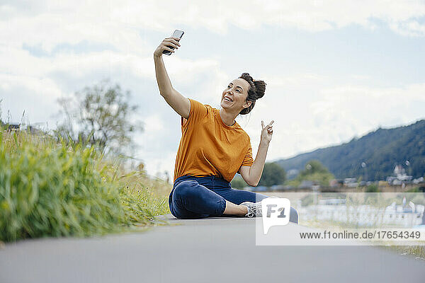 Smiling woman gesturing pace sign taking selfie on wall
