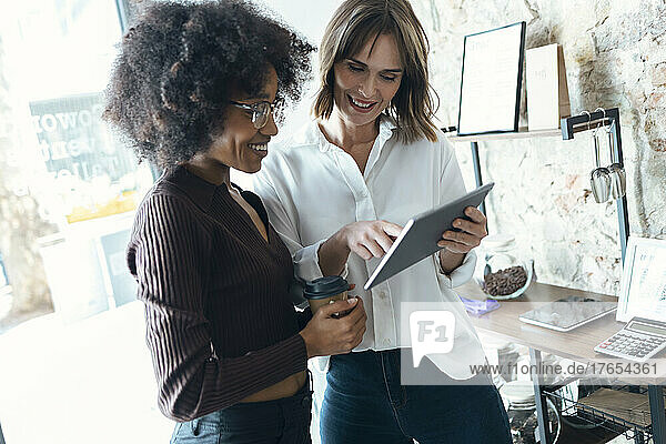 Smiling businesswoman sharing tablet PC with colleague in office