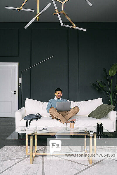 Freelancer working on laptop sitting cross-legged on sofa at home