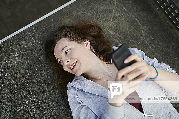 Young woman lying on table tennis table holding smartphone