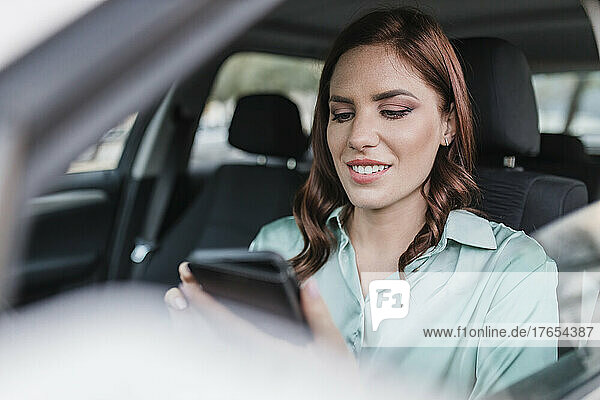 Smiling businesswoman using smartphone in car